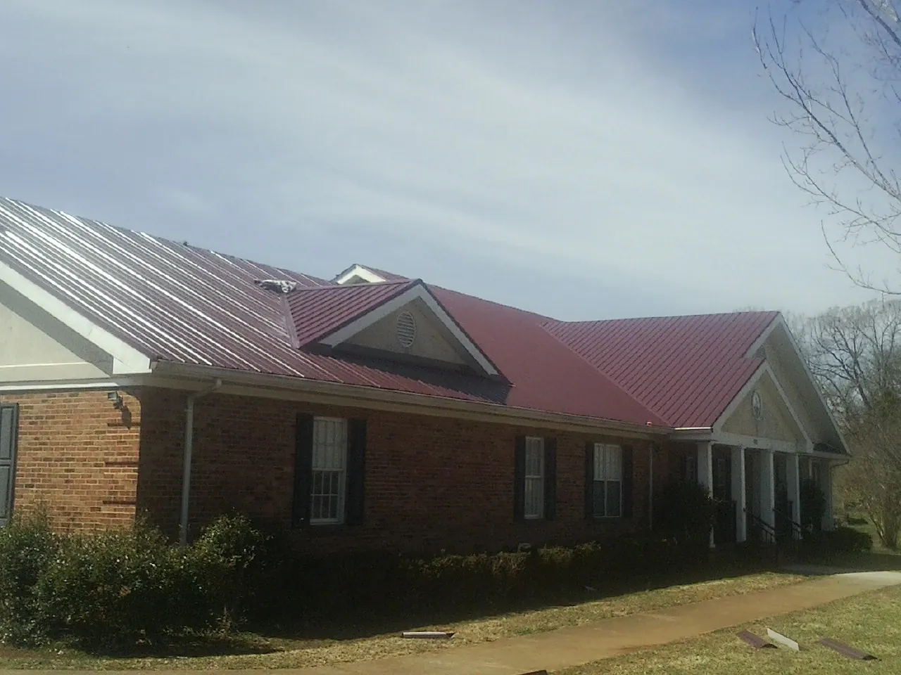 Red metal roof with gabled entries on a long brick building, from a Hail Damage Roof Repair job in Arvilla