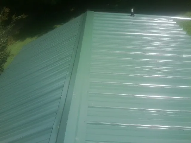 New green metal panels meeting at the ridge of a roof — Flat Roof Repair work by our crew in Arvilla
