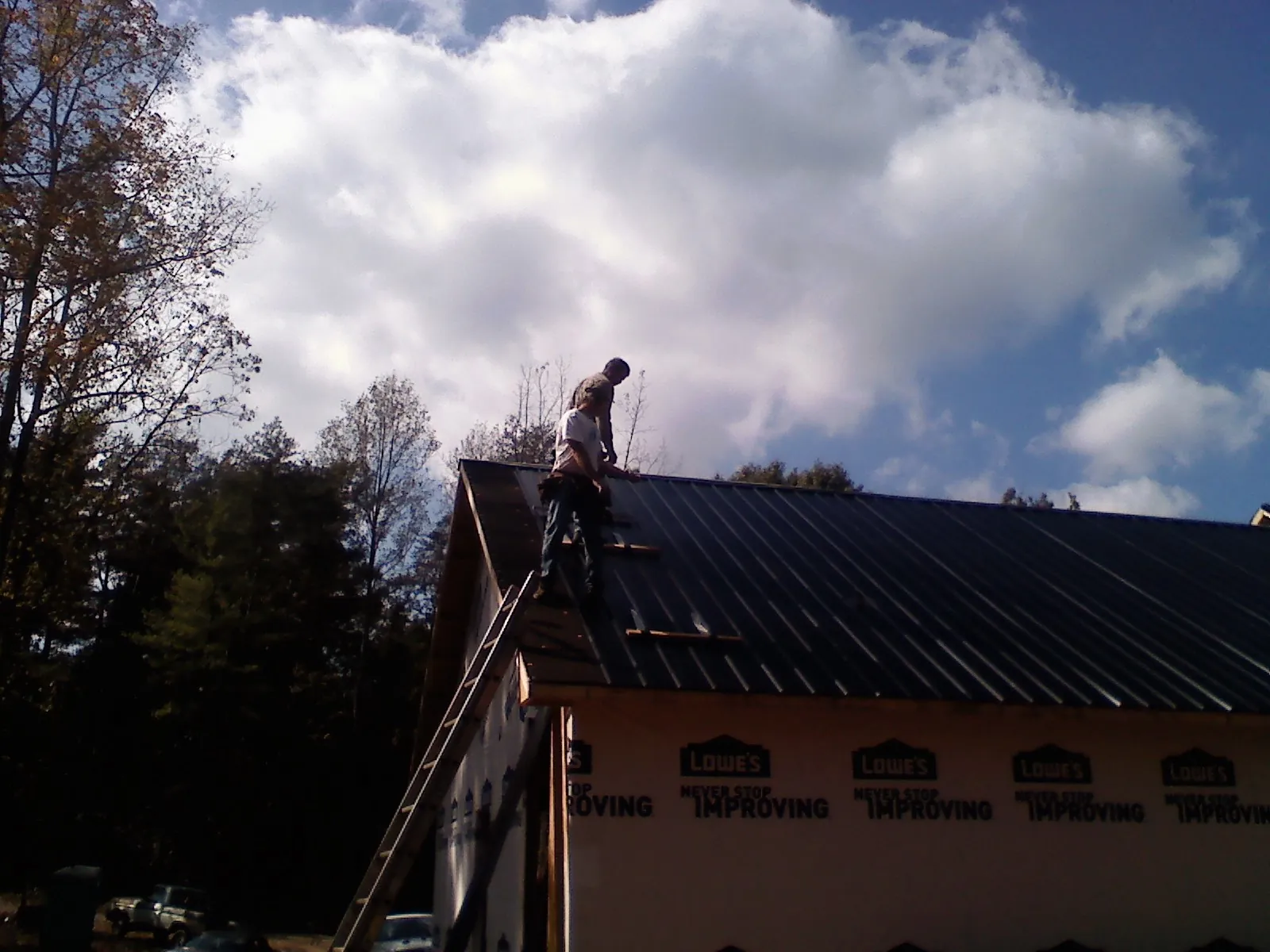 Roofer fastening dark metal panels high against a cloudy sky, from a Roof Inspection job in Arvilla