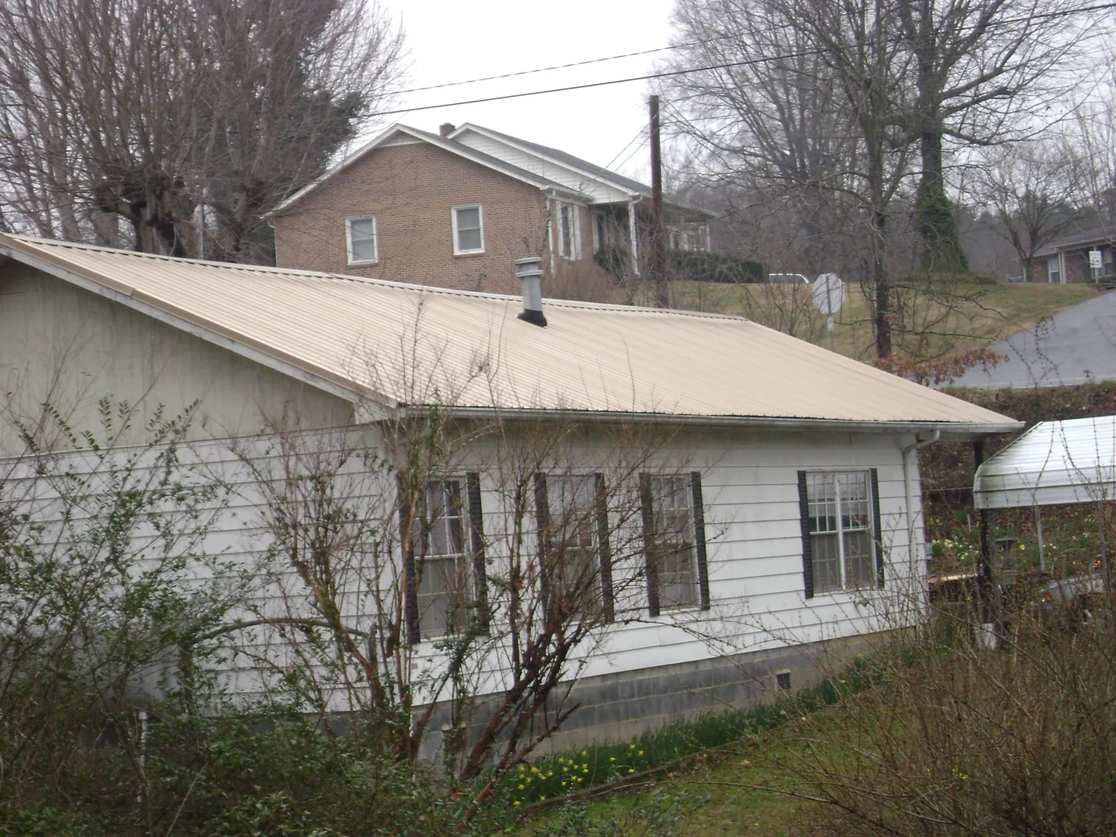 Tan metal roof on a white sided house set into a hillside — Commercial Roofing by Roofing Brothers in Arvilla